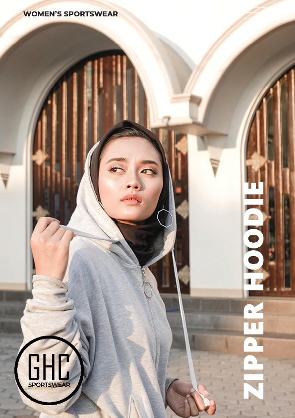 A woman wearing a custom women's zipper hoodie in light gray, featuring a stylish and functional design, standing in front of an arched building. Available at ghcsportswear.com.