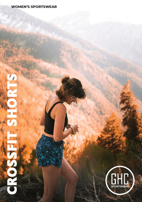 A woman wearing custom women's crossfit shorts from GHC Sportswear, standing on a mountain trail with scenic views of a forest and mountains in the background.