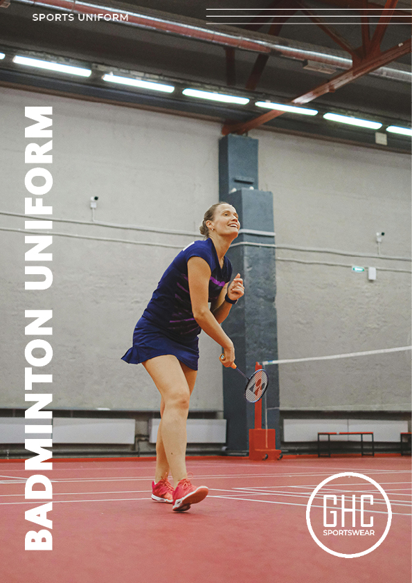 A badminton player wearing a custom badminton uniform in blue, holding a racket and preparing to serve on an indoor court. Available at ghcsportswear.com.