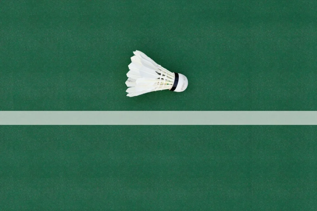 Life of a badminton shuttlecock shown on an indoor court with a ruffled feather shuttle, custom badminton apparel, and a player lunging during a rally.
