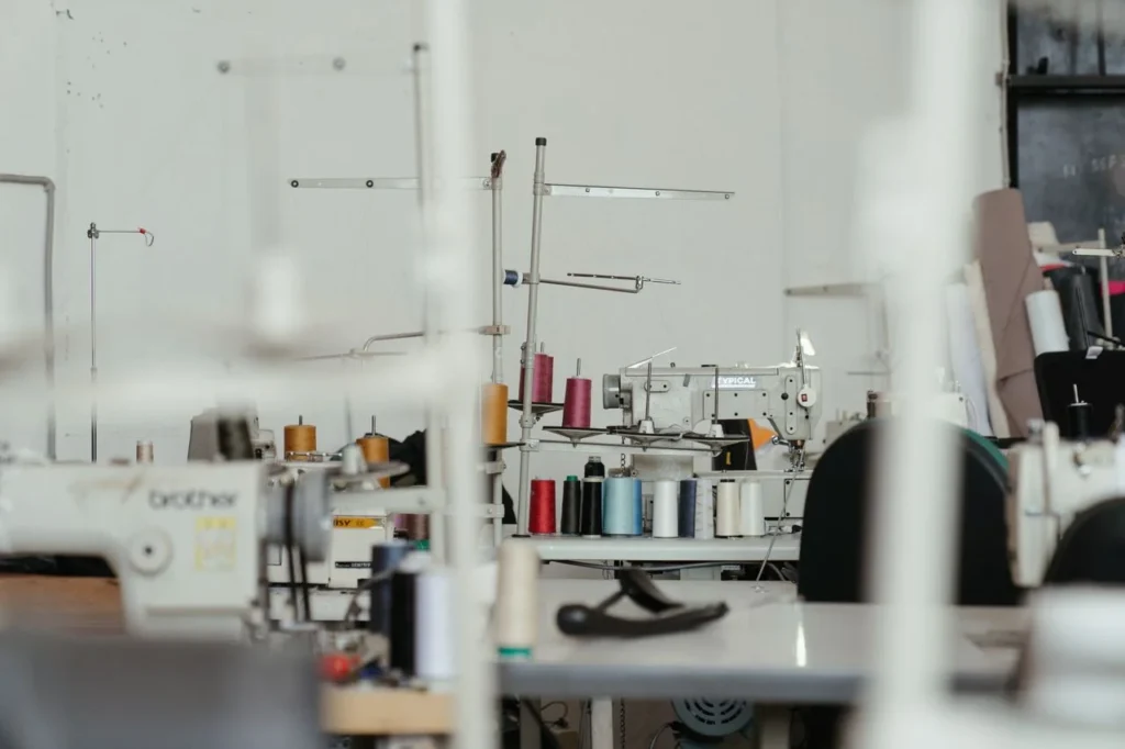 Apparel manufacturing product planning table with tech packs, fabric swatches, size charts, trim cards, sample garments, QC checklist, and bulk production planning.