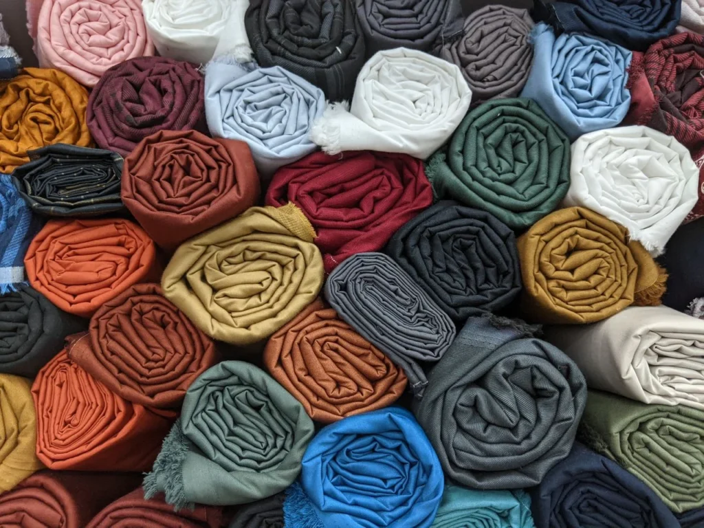 Fabric and trim sourcing table with fabric swatches, lab dips, zippers, thread, elastic, labels, quality tests, BOM, and bulk apparel planning.