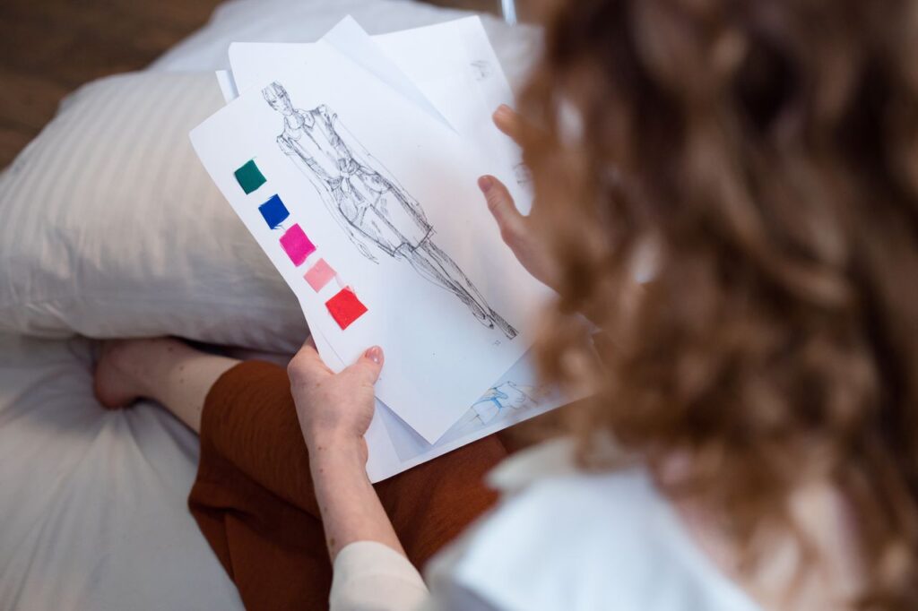 Designer reviewing garment sketches and fabric samples for apparel tech pack planning.